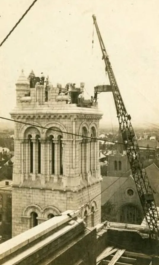 Workmen and a lattice crane atop a stone bell tower of the Cathedral Basilica of Saint Louis during its construction, about 1910