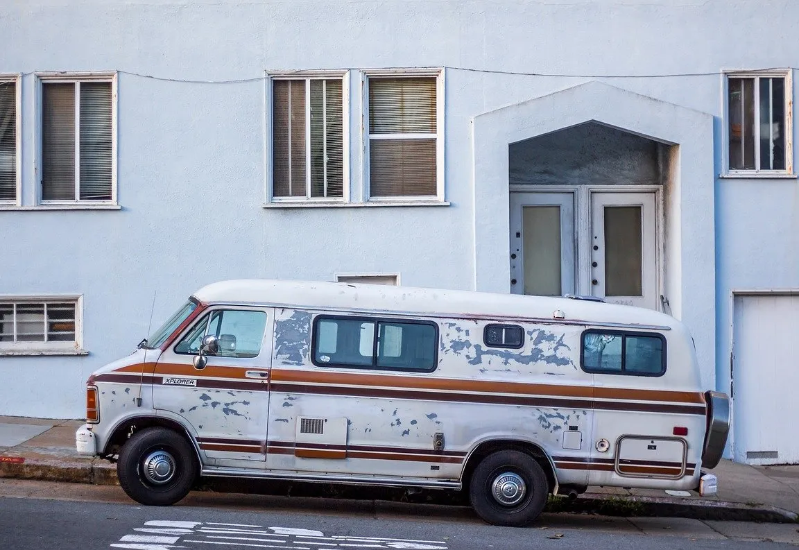 A worn white work van with brown stripes parked at the curb on a city street