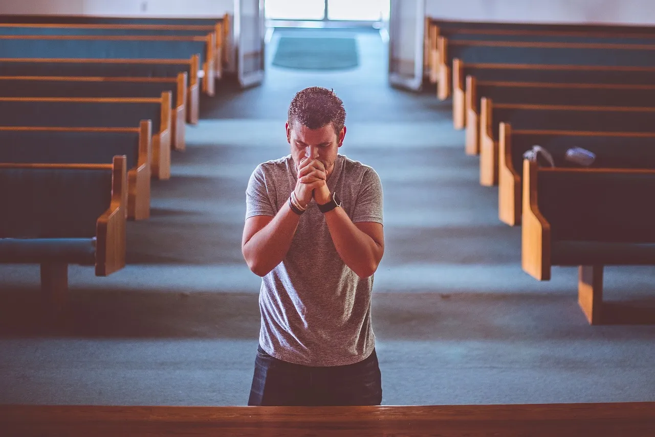 A man kneeling alone in prayer between the pews of an empty church